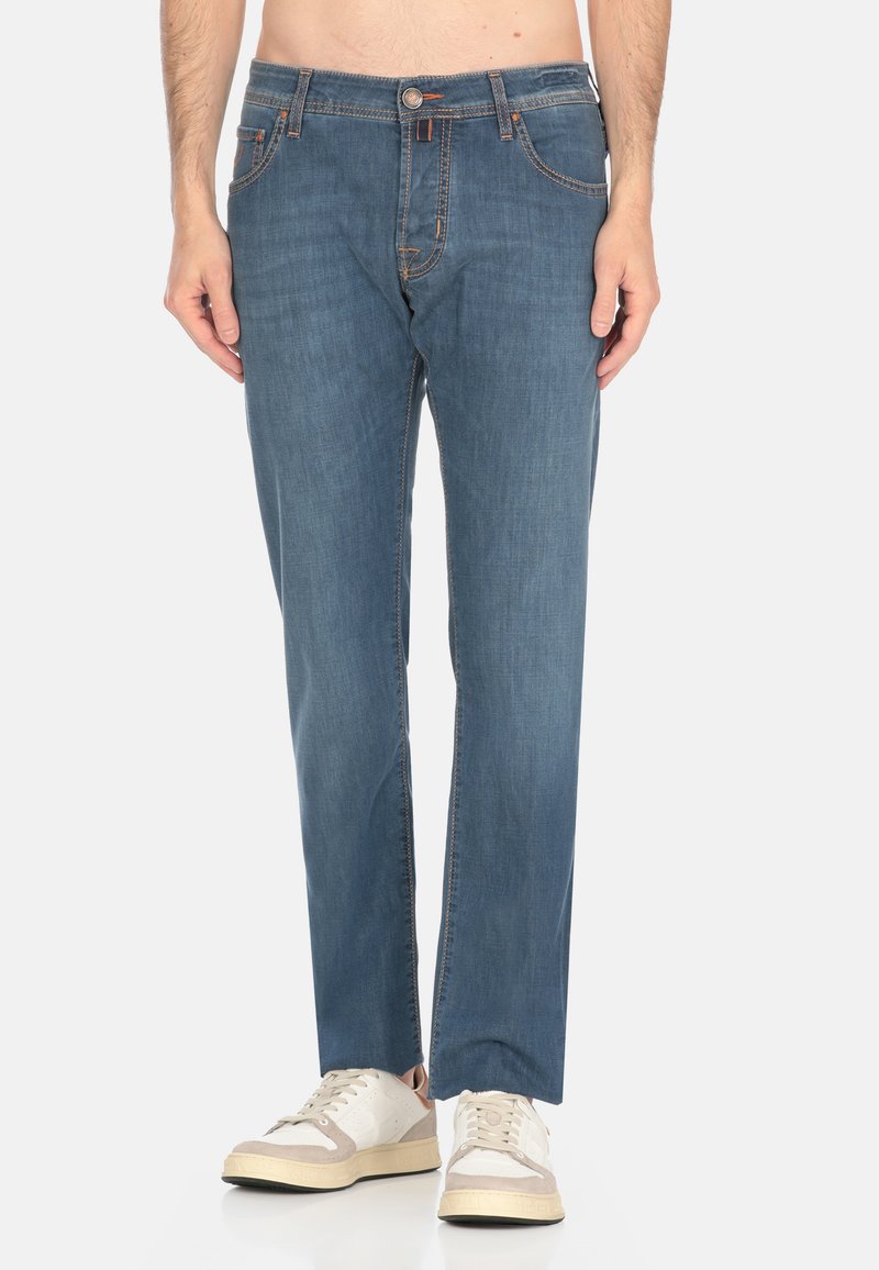 Jeans in denim blu con una vestibilità dritta, caratterizzati da cuciture arancioni, chiusura frontale con bottone e due tasche laterali. Indossati con sneaker di colore chiaro.