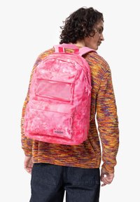 Rosa tie-dye ryggsäck med flera fack, nätficka och justerbara remmar. Har en märkesetikett i framkant. Tyget har en mjuk textur.