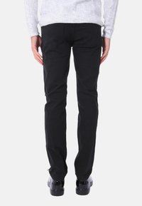 Pantaloni neri con design a gamba dritta, realizzati in cotone, con tasche posteriori e cuciture in contrasto. Indossati con un leggero maglione a trecce.