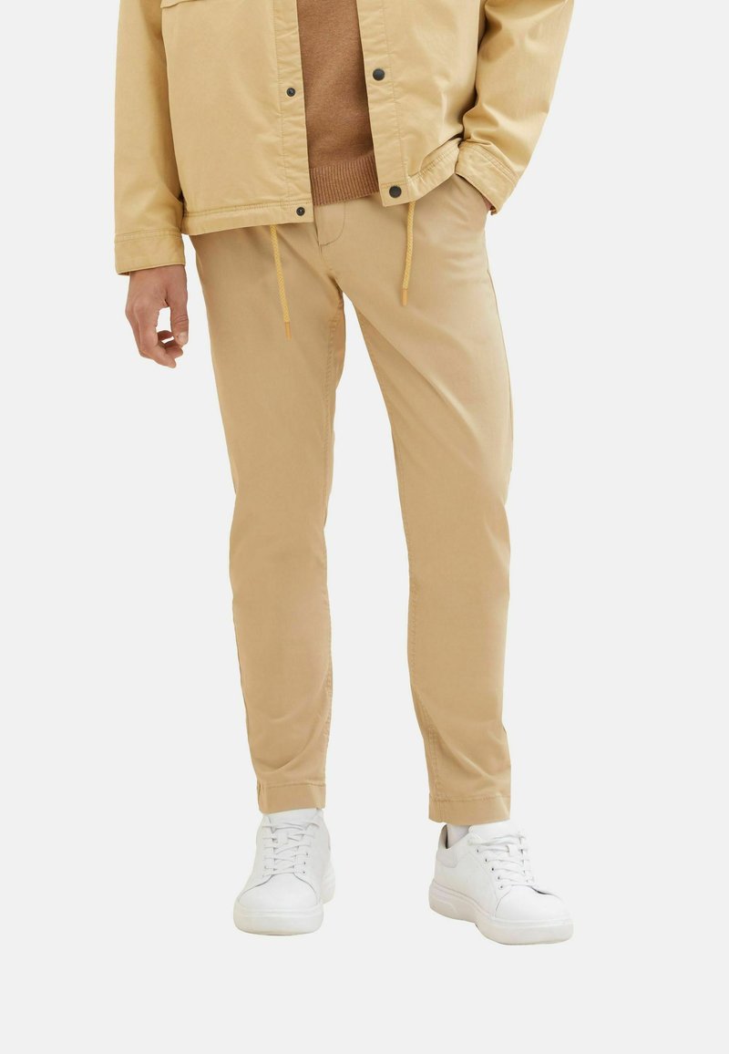 Beiga bomullschinos med avsmalnande ben, elastisk dragsko i midjan och sidofickor, tillsammans med vita sneakers.