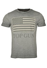 Grå t-shirt tillverkad av mjukt material, med en stor, bleknad amerikansk flagg-grafik och "TOP GUN"-text i fet stil, i kontrasterande färg.