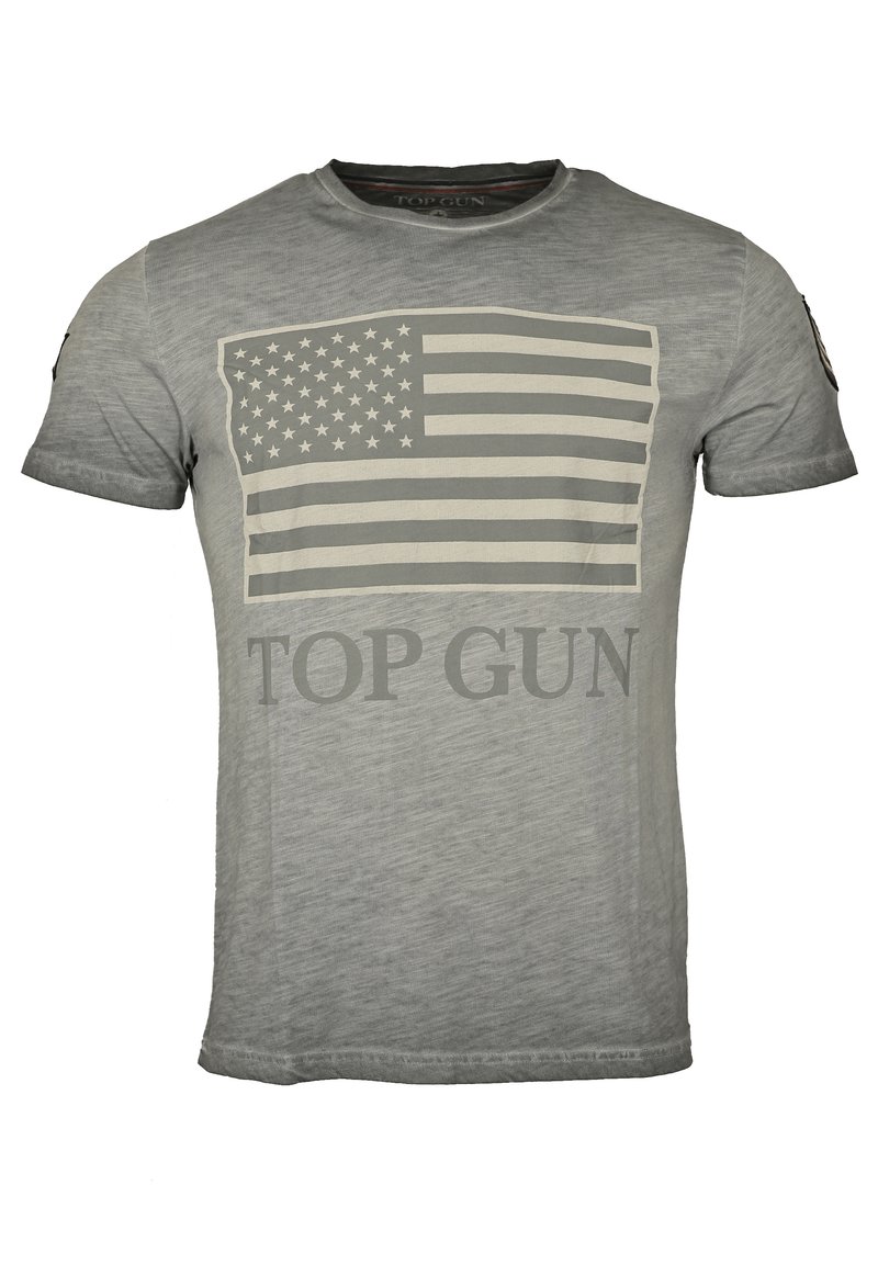 Grå t-shirt tillverkad av mjukt material, med en stor, bleknad amerikansk flagg-grafik och "TOP GUN"-text i fet stil, i kontrasterande färg.