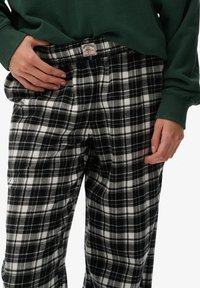 Czarno-białe flanelowe spodnie w kratę z elastycznym pasem, prezentujące miękką fakturę oraz metkę z przodu przy talii.