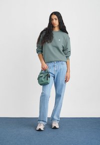 Szürke kapucnis pulóver kis logóval, világoskék csíkos bőrnadrág, világoszöld táska cipzárokkal, és szürke sportcipő kiegészítőkkel.