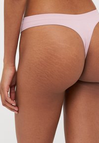 Roze geribbelde string met een smalle tailleband, met een zicht op de achterkant en huidtextuur, inclusief zichtbare striae.