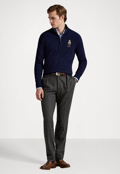 Navy knit pullover with a quarter zip and logo, paired with gray pleated trousers and brown leather shoes, featuring a collared shirt underneath.