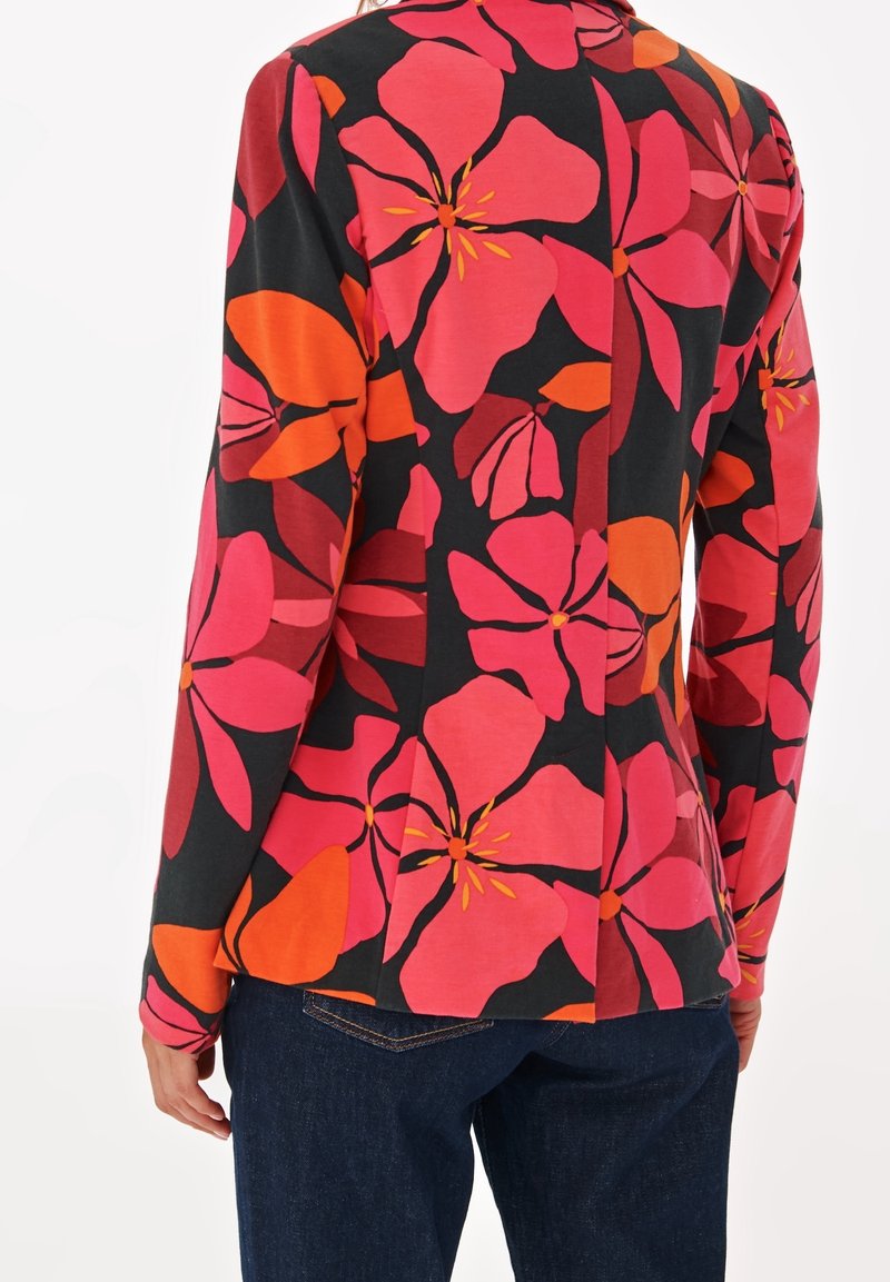 Femme portant une chemise à manches longues avec de grands motifs floraux roses et orange sur fond noir, associée à un jean bleu foncé.