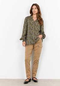 Long-sleeve, patterned blouse in dark olive-green with subtle floral design, paired with khaki pants featuring side pockets and a tapered fit.