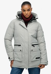 Jasnoszary ocieplany parka z kapturem, czarnymi dodatkami, bocznymi kieszeniami i zamkiem błyskawicznym z przodu. Posiada wysoki kołnierz i regulowane mankiety.