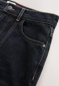 Sötétkék farmernadrág kontrasztos sárga varrással, elülső zsebbel és fém gombbal. Simább textúrájú és klasszikus szabású.