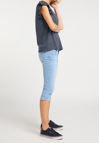 Mörkblå prickig topp med volangärmar, ljusblå cropped jeans med rå kant och mörkblå sneakers med vita sulor. Sidovy av outfiten.