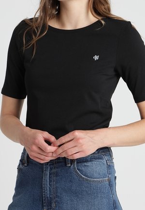 Sort t-shirt med korte ærmer, rund halsudskæring og lille broderet logo på brystet, kombineret med høj-taljede blå cowboybukser.