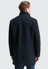 Abrigo de mezcla de lana en color navy con un ajuste entallado, cuello alto y hombros estructurados. Textura suave y líneas limpias, con una abertura en la parte posterior.