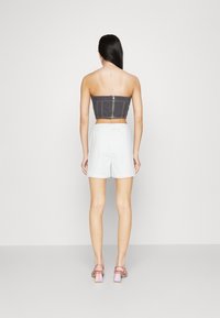 Černý denimový cropped top se zipovým zapínáním, spárovaný s bílými texturovanými šortkami. Model, který má na sobě růžové sandály na podpatku. Hladké pozadí.