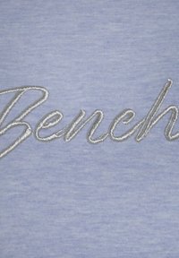 Tejido azul claro con texto bordado en plata que dice "Banco". La textura parece suave con un sutil patrón jaspeado.