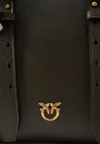 Zwarte leren handtas met een getextureerd oppervlak, een vogel-embleem in goudkleurige hardware en decoratieve uitsparingen langs de banden.