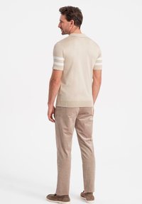 Beige stickad polo skjorta med vita ränder på ärmarna, kombinerad med ljusbruna manchesterbyxor och beige sneakers.