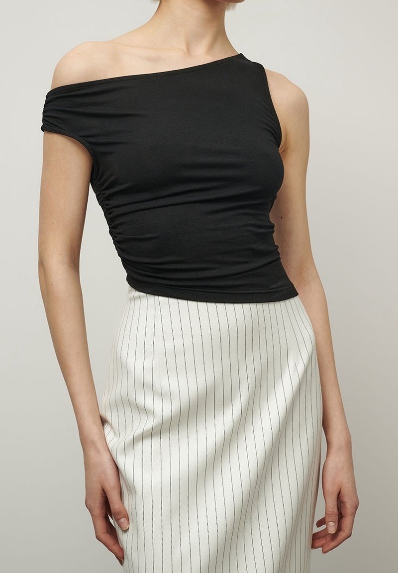 Mustat, olkapäältä avonaista toppia, joka on valmistettu joustavasta kankaasta ja jossa on poimittu yksityiskohta, yhdistetty pystysuoraraidalliseen valkoiseen hameeseen, luoden istuvan siluetin.