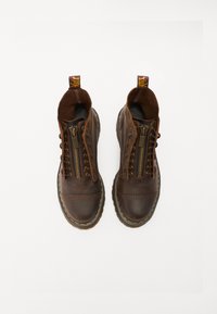 Des bottes de cheville en cuir marron présentent une fermeture zippée, des coutures jaunes contrastantes et une languette au talon. Tige texturée pour durabilité.