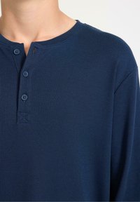 Marineblauwe langwerpige henley-shirt met een ribbelstructuur, voorzien van drie knopen en een ronde kraag. Eenvoudig ontwerp zonder patroon.