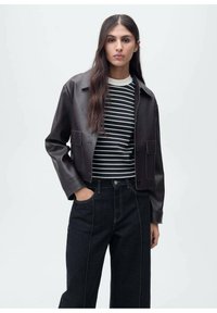 Brun læder cropped jakke med krave-design, parret med en sort-hvid stribet skjorte og mørke højtaljede jeans.