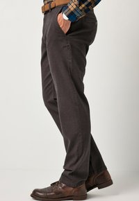 Pantaloni in cotone grigio scuro con design a gamba dritta, tasche laterali e una cintura marrone; indossati con scarpe in pelle marrone.