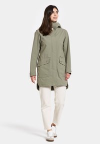 Kaki regnkappa med huva, två stora framfickor och tryckknappar. Matchad med krämfärgade byxor och vita sneakers.