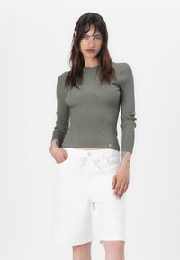 Maglia a maniche lunghe a coste verde oliva con una silhouette aderente, abbinata a pantaloni corti bianchi su misura con vita regolabile e tasche laterali.