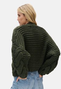 Gruby, oliwkowozielony sweter z dzianiny z warkoczowymi rękawami i teksturowanym korpusem. Posiada prążkowany dół, zapewniający luźne dopasowanie.