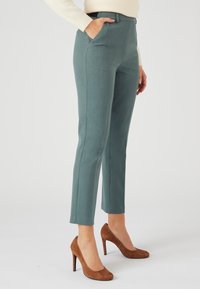 Lichtblauwe op maat gemaakte broek met een rechte pijp. Voorzien van zijzakken en een subtiele textuur. Gecombineerd met bruin suède hoge hakken.