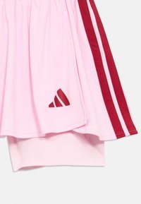 Ροζ αθλητική φούστα με κόκκινες πλευρικές ρίγες, κατασκευασμένη από λείο ύφασμα. Φέρει λογότυπο Adidas σε κόκκινο στην κάτω αριστερή πλευρά. Περιλαμβάνει εσωτερικό σορτς.