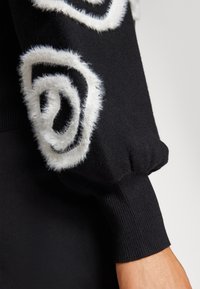 Black knit sweater with large white fluffy spiral patterns on the sleeves. Features ribbed cuffs, highlighting texture and design detail.