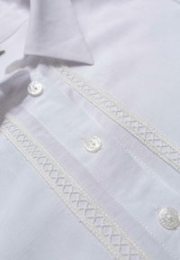 Chemise blanche habillée avec bordure de dentelle verticale brodée et boutons nacrés sur le devant, montrant les détails du col et de la patte de boutonnage.