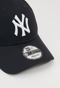 Navy cap made of cotton with a curved brim, featuring white embroidered 'NY' logo and a circular tag stating '9FORTY ADJUSTABLE'.