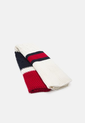 Gefalteter Strickschal mit Zopf- und Rippenmustern in Rot, Weiß und Marineblau auf weißem Hintergrund.