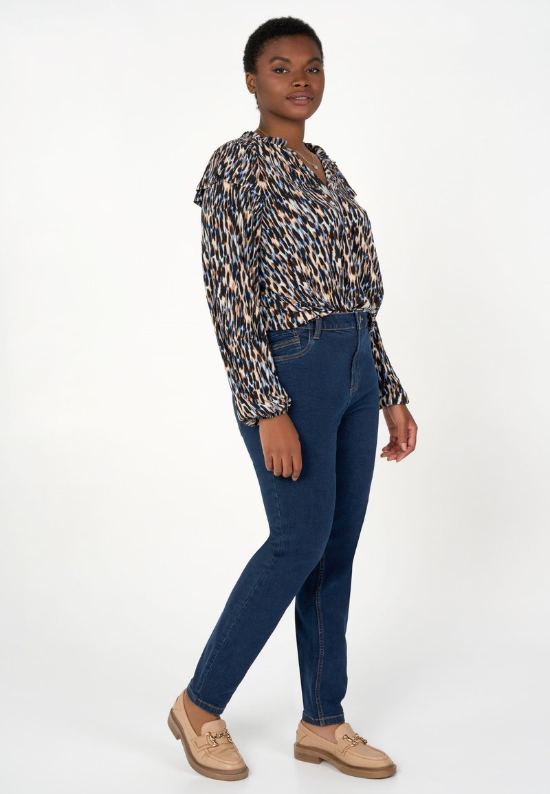 Blouse légère imprimée dans des teintes de bleu, marron et crème ; jeans en denim bleu foncé décontractés ; mocassins beiges avec des accents décoratifs en métal.