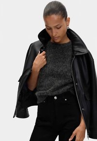 Černá kožená bunda se širokým límcem, v kombinaci s tmavě šedým chlupatým svetrem. Oblečení doplňují úzké černé džíny a stříbrné kovové detaily.