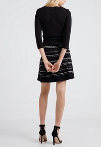Schwarzes Cropped-Top mit Dreiviertelärmeln und einem Reißverschluss hinten, kombiniert mit einem schwarzen Rock mit weißen horizontalen Streifen. Schwarze High-Heelsandalen.