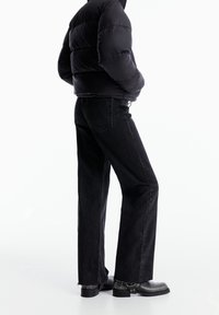 Doudoune noire, jean noir à jambes larges et bottes noires épaisses. Le jean a une bordure brute et quatre poches, tandis que la doudoune possède une fermeture éclair.