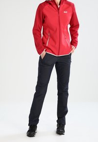 Rød softshelljakke med lynlåslukning, kombineret med marineblå bukser med cargolommer. Sorte vandresko fuldender outfittet.