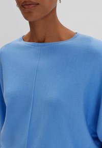 Maglione blu lavorato a maglia con una vestibilità ampia, scollatura rotonda e maniche corte. Il materiale è morbido con una texture liscia e dettagli di cucitura discreti.