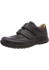 Chaussure en cuir noir avec deux bandes velcro, bout arrondi, intérieur rembourré, semelle texturée et couture discrète sur le dessus.