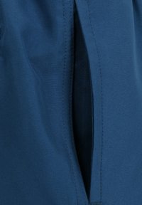 Blauer Stoff mit einer glatten Textur, der über eine seitliche Taschenöffnung verfügt. Die Nähte sind sauber und gleichmäßig und zeigen eine qualitativ hochwertige Verarbeitung.