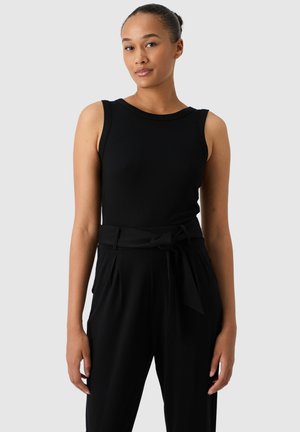Top senza maniche nero a costine con scollatura a girocollo, abbinato a pantaloni neri a vita alta con una cintura annodata in evidenza. Tessuto morbido.