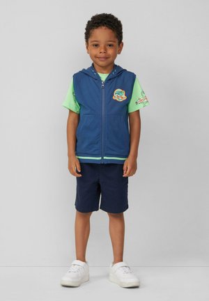 Marinefarbener ärmelloser Hoodie mit durchgehendem Reißverschluss, grünes T-Shirt mit kurzen Ärmeln, marinefarbene Shorts und weiße Sneakers. Verfügt über ein gesticktes Emblem.