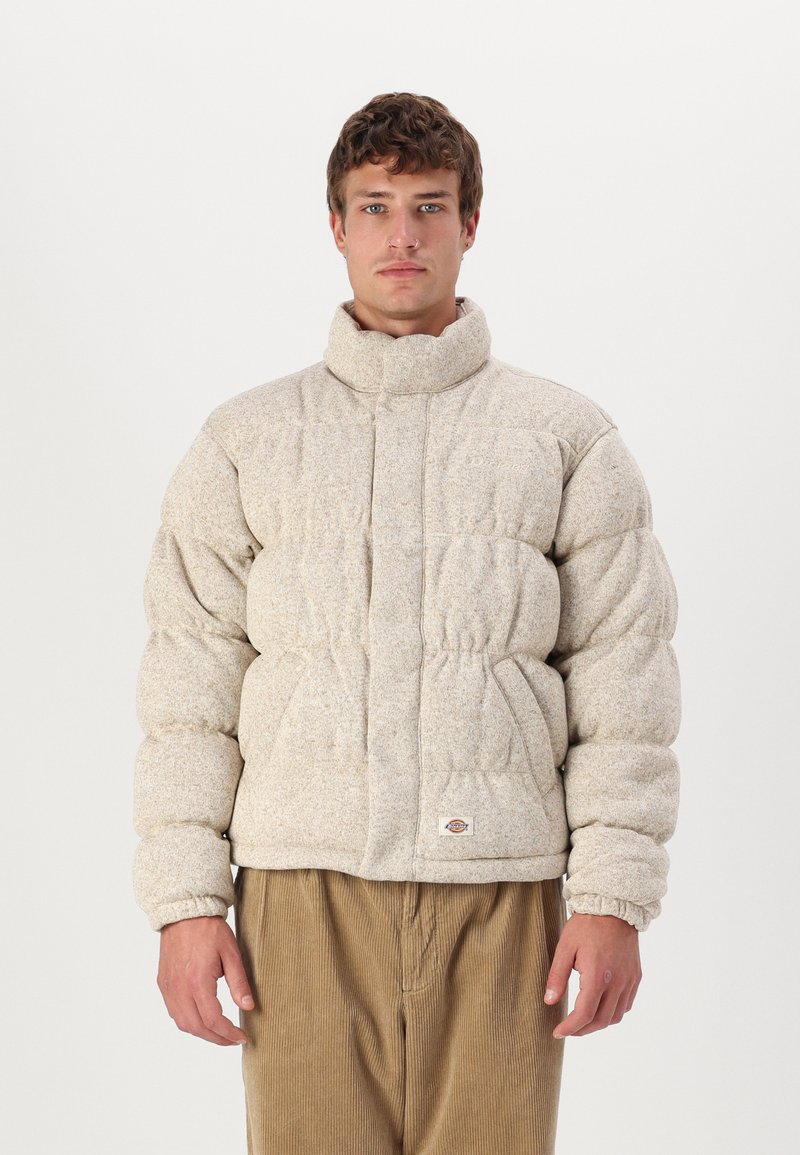 Beige pufferjakke med høj krave og elastiske manchetter. Tekstureret stof med en quiltet design og to sidelommer. Bæres over fløjlsbukser.