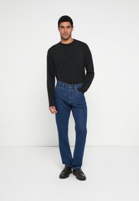 Melna krekla ar garām piedurknēm un zili taisna piegriezuma džinsi ar klasisku piecu kabatu dizainu un smalkām šuvju detaļām. Brūnas kurpes.