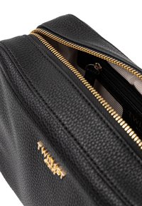 Borsa nera in pelle con texture granulosa, caratterizzata da una cerniera e dettagli in oro. Interno con fodera beige e scomparti per carte.