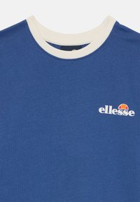 Camiseta de manga corta azul hecha de suave algodón, con un cuello redondo crema y un logotipo de marca blanco con un acento de color.