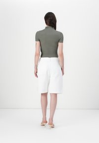 Olivenfarget ribbestrikket topp med kort erme, parret med hvite skreddersydde shorts med baklommer og rett ben-design. Elegante heler på slep.